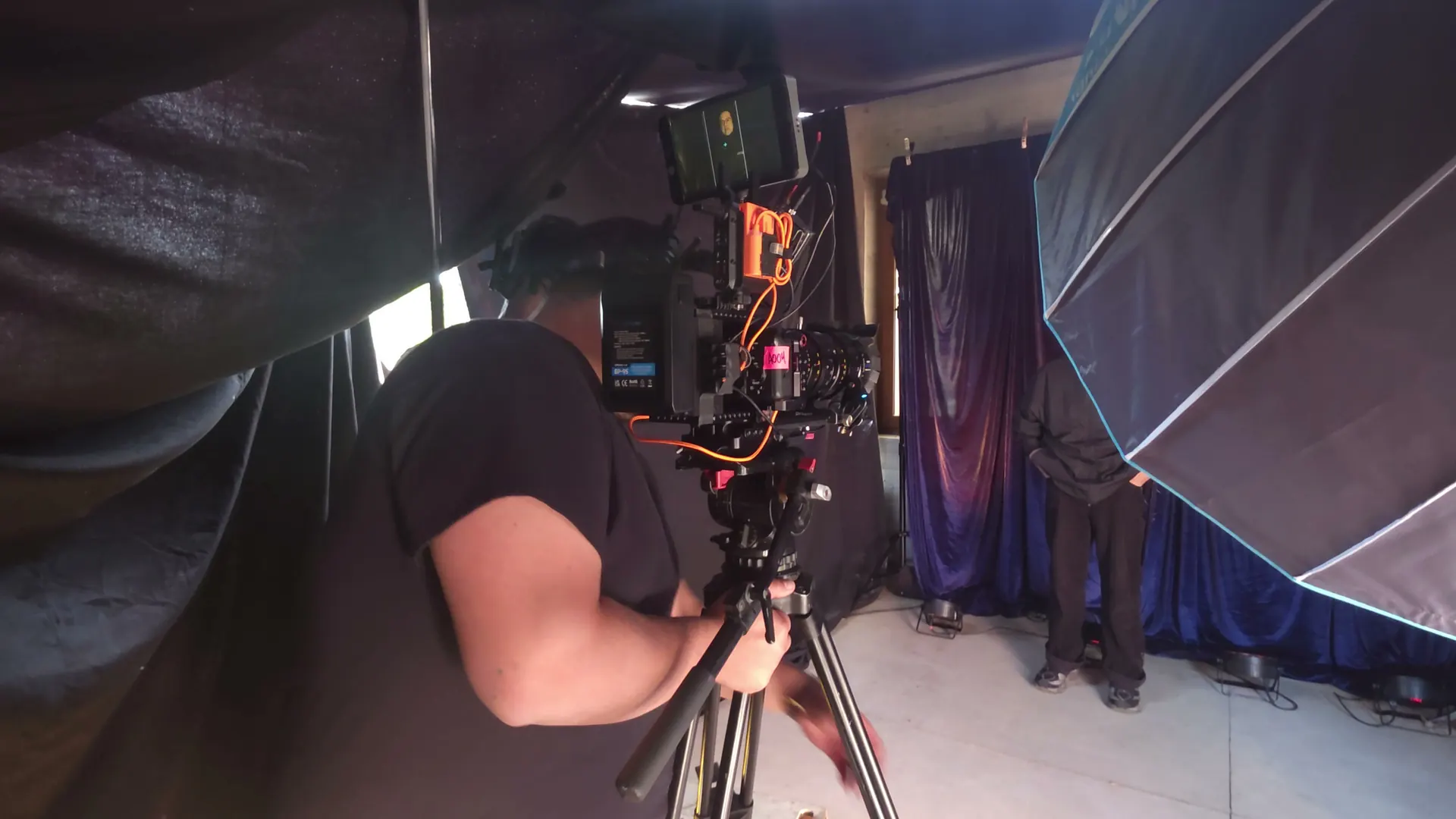 Rig de cámara con monitor y cables naranjos en un estudio en penumbra.